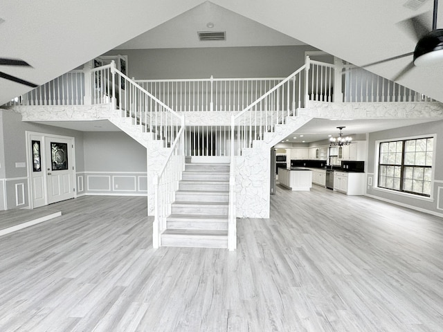 staircase featuring a high ceiling, hardwood / wood-style floors, and ceiling fan with notable chandelier