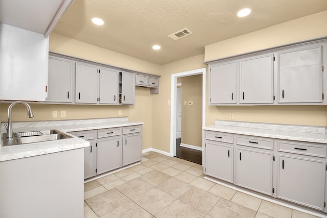 kitchen with gray cabinets, sink, light tile patterned flooring, and a textured ceiling