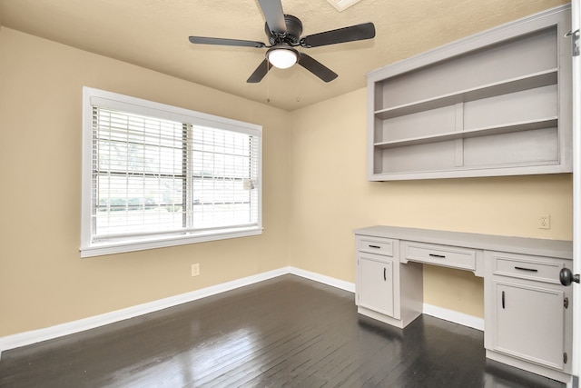 unfurnished office with dark hardwood / wood-style flooring, built in desk, and ceiling fan