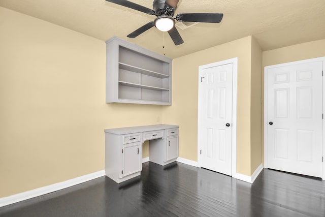 unfurnished office with dark hardwood / wood-style floors, ceiling fan, built in desk, and a textured ceiling