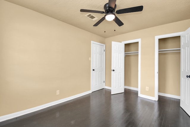 unfurnished bedroom featuring a textured ceiling, ceiling fan, dark wood-type flooring, and two closets