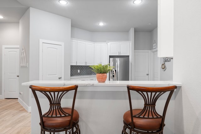 kitchen featuring light wood-type flooring, stainless steel fridge with ice dispenser, white cabinetry, and a breakfast bar