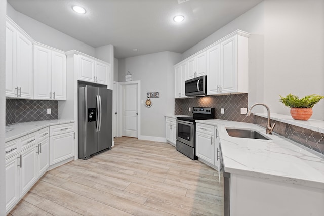 kitchen with light hardwood / wood-style floors, sink, light stone countertops, white cabinetry, and appliances with stainless steel finishes