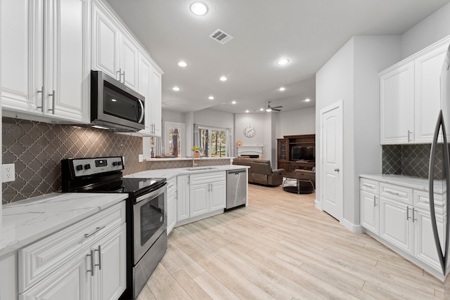 kitchen with stainless steel appliances, ceiling fan, light stone countertops, white cabinetry, and light wood-type flooring