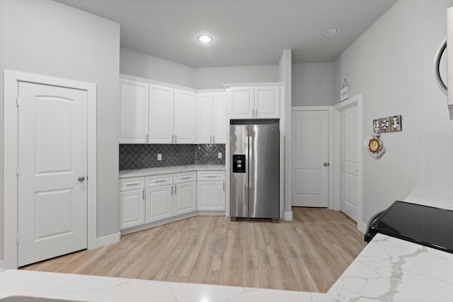 kitchen with light stone counters, stainless steel fridge with ice dispenser, backsplash, white cabinetry, and light hardwood / wood-style flooring