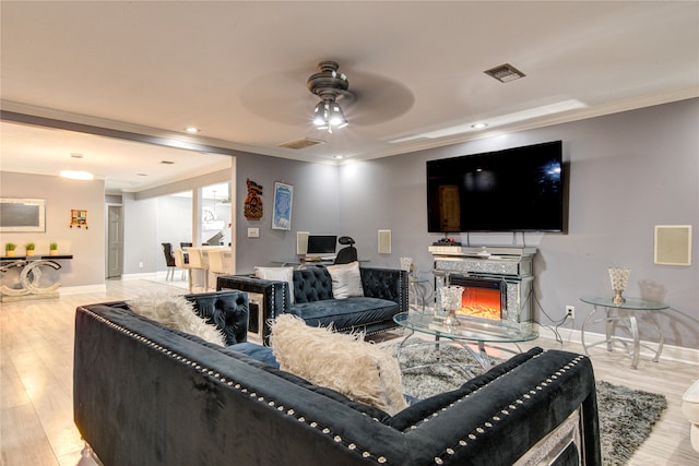 living room featuring ceiling fan, ornamental molding, and light hardwood / wood-style flooring