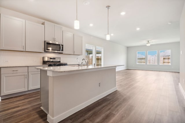 kitchen featuring tasteful backsplash, ceiling fan, appliances with stainless steel finishes, dark wood-style flooring, and a kitchen island with sink