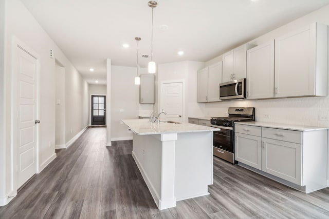 kitchen featuring dark wood finished floors, a center island with sink, appliances with stainless steel finishes, a sink, and baseboards