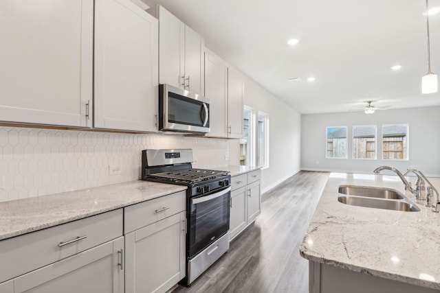 kitchen with a ceiling fan, appliances with stainless steel finishes, a sink, light wood-style floors, and backsplash