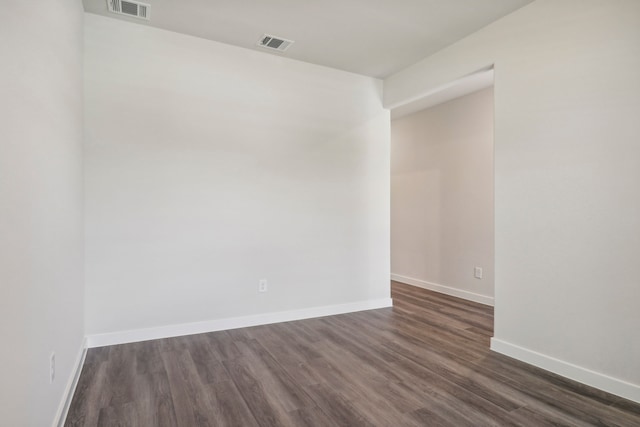 spare room featuring dark wood-style flooring, visible vents, and baseboards