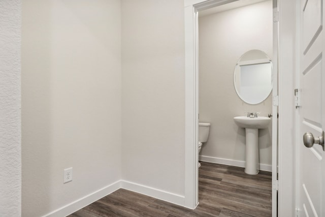 half bathroom featuring a sink, toilet, baseboards, and wood finished floors