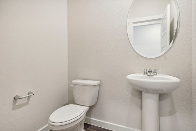 half bath featuring baseboards, toilet, and wood finished floors