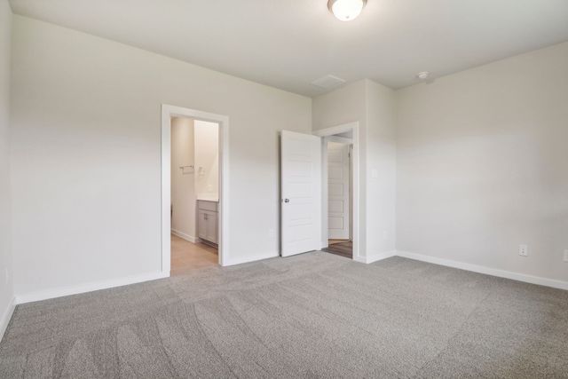 unfurnished bedroom featuring baseboards, ensuite bath, and light colored carpet