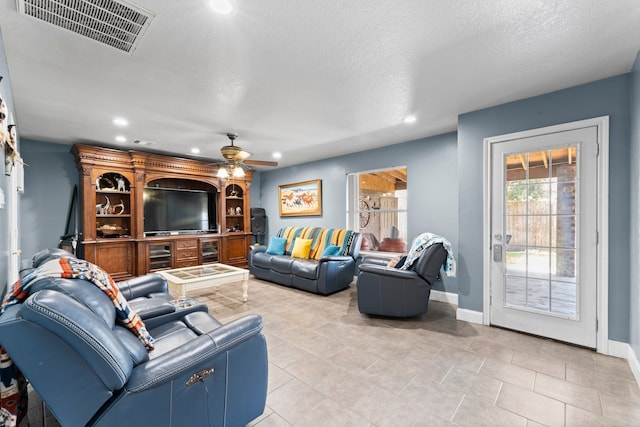 living room with a textured ceiling, light tile patterned floors, and ceiling fan