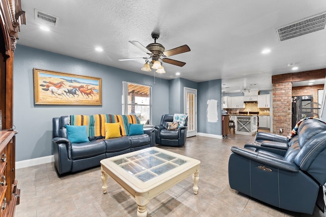 tiled living room with a textured ceiling, ceiling fan, and decorative columns