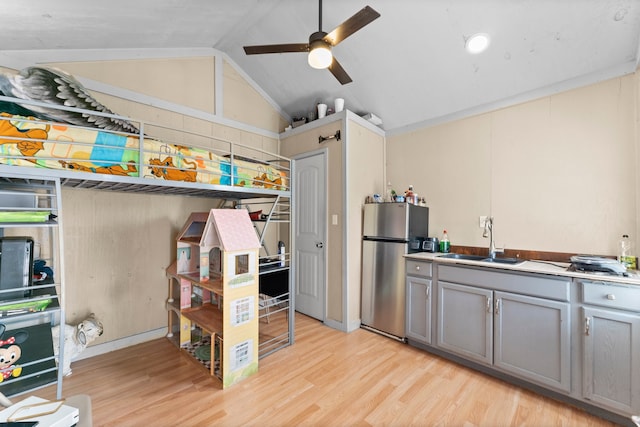 kitchen with gray cabinetry, stainless steel fridge, light wood-type flooring, sink, and vaulted ceiling