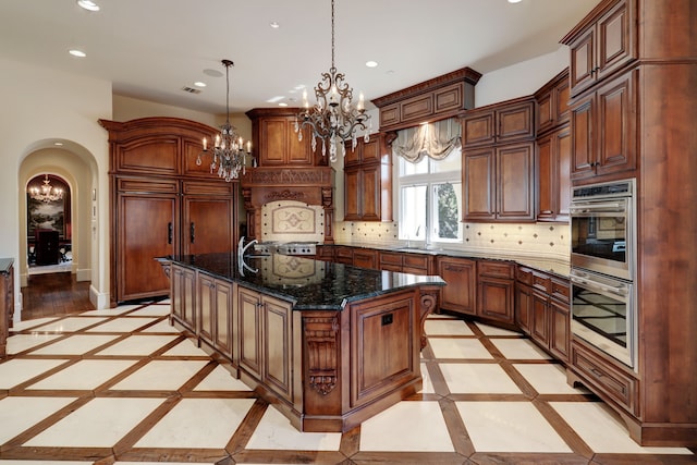 kitchen with dark stone counters, backsplash, pendant lighting, sink, and a kitchen island with sink