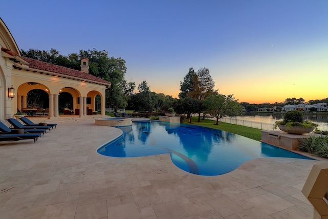 pool at dusk featuring a water view, an in ground hot tub, and a patio area