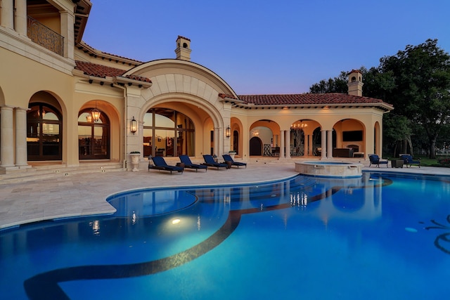 pool at dusk featuring an in ground hot tub and a patio area