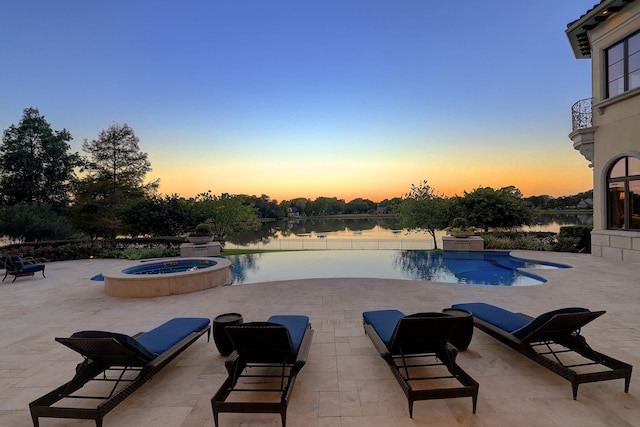 pool at dusk featuring a water view, a patio, and an in ground hot tub