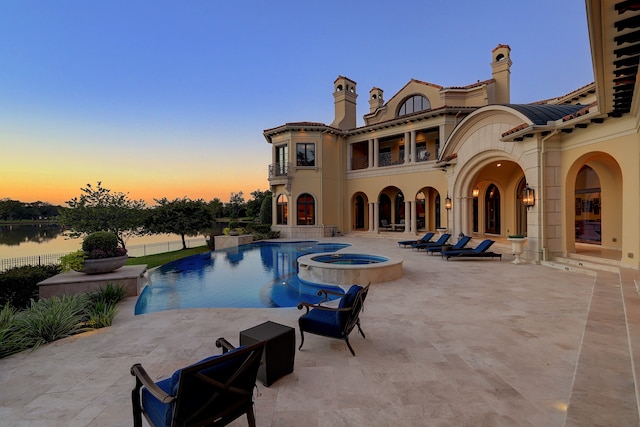 pool at dusk featuring a patio area, a water view, and an in ground hot tub