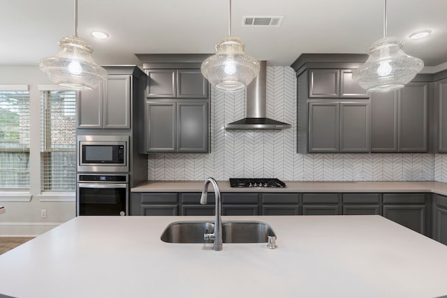 kitchen with pendant lighting, stainless steel appliances, sink, and wall chimney range hood