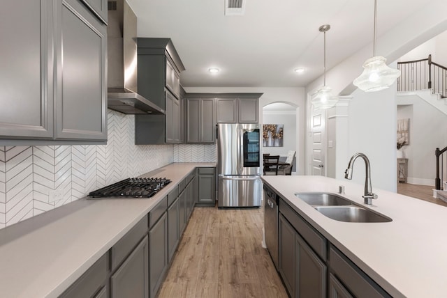 kitchen featuring light wood-type flooring, appliances with stainless steel finishes, decorative light fixtures, sink, and wall chimney exhaust hood