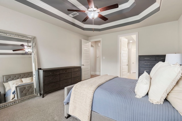 bedroom featuring ornamental molding, connected bathroom, a tray ceiling, light colored carpet, and ceiling fan