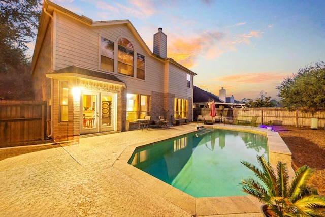 back house at dusk with a fenced in pool, a patio area, and french doors