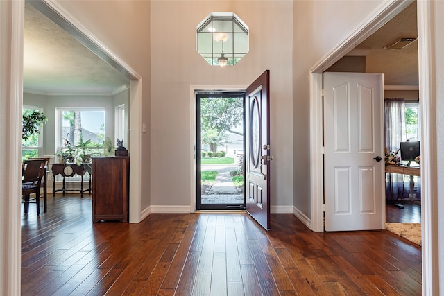 foyer with dark wood-type flooring, plenty of natural light, a textured ceiling, and crown molding