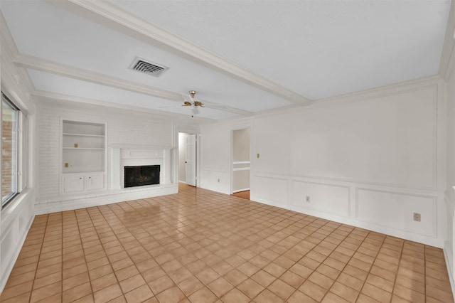 unfurnished living room with a brick fireplace, built in shelves, light tile patterned floors, ceiling fan, and crown molding