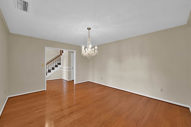 spare room featuring hardwood / wood-style floors, crown molding, and an inviting chandelier