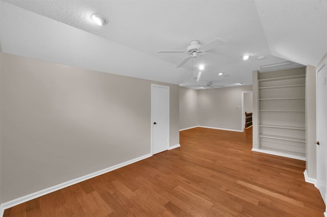 interior space with built in shelves, a textured ceiling, vaulted ceiling, hardwood / wood-style flooring, and ceiling fan