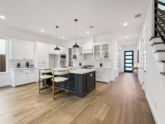 kitchen featuring custom exhaust hood, a kitchen island with sink, white cabinets, light hardwood / wood-style flooring, and appliances with stainless steel finishes