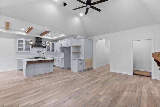 kitchen featuring custom exhaust hood, a kitchen island, white cabinetry, light wood-type flooring, and decorative light fixtures