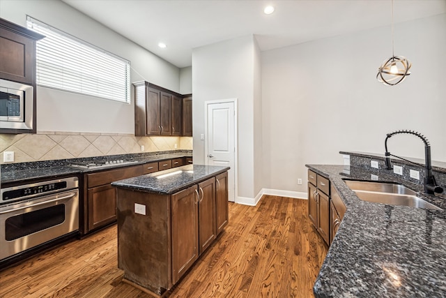 kitchen featuring a center island with sink, sink, appliances with stainless steel finishes, dark hardwood / wood-style floors, and decorative light fixtures