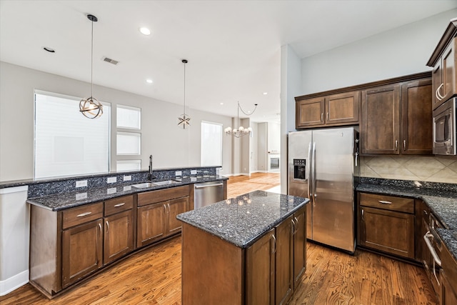 kitchen with appliances with stainless steel finishes, sink, wood-type flooring, and hanging light fixtures