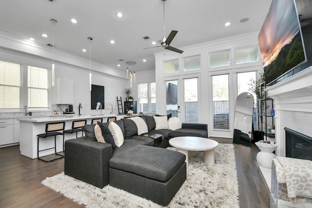 living room with dark wood-type flooring, a tiled fireplace, ceiling fan, and ornamental molding