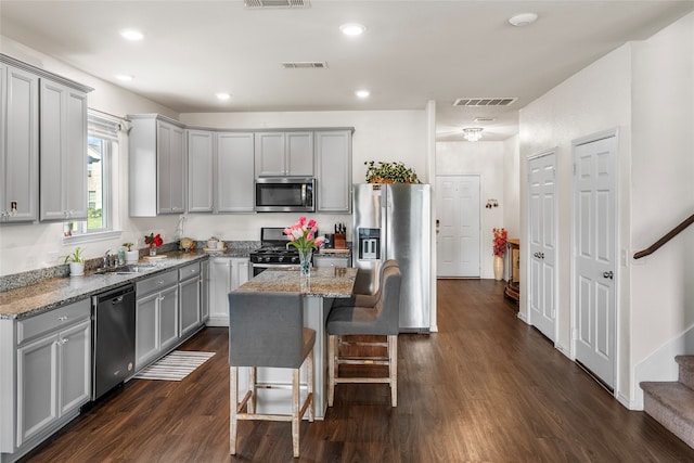 kitchen featuring gray cabinets, dark stone countertops, a kitchen island, and appliances with stainless steel finishes