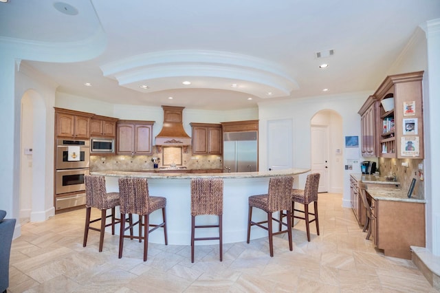 kitchen featuring tasteful backsplash, custom range hood, built in appliances, and a kitchen island with sink