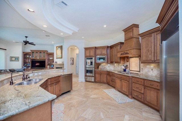 kitchen featuring built in appliances, sink, light stone counters, tasteful backsplash, and ceiling fan