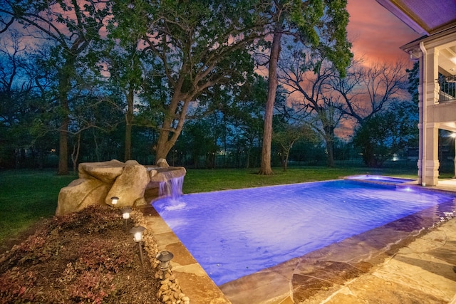 pool at dusk featuring a lawn, pool water feature, and a patio area