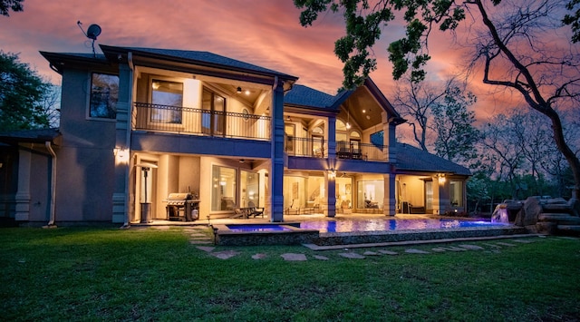 back house at dusk with a lawn, a balcony, pool water feature, a patio, and a pool with hot tub