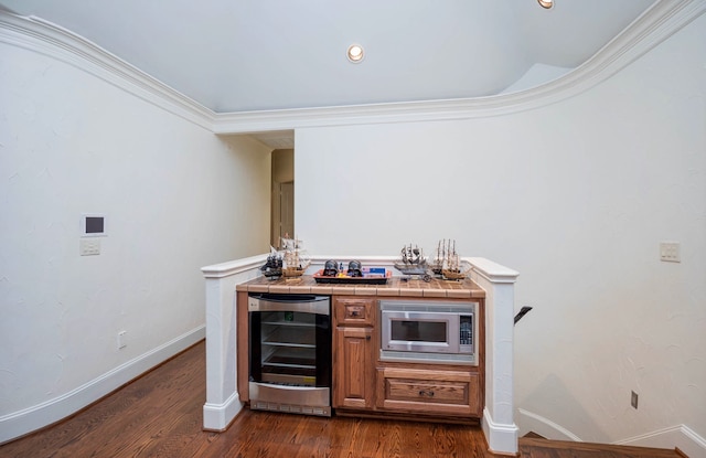 bar featuring wine cooler, ornamental molding, stainless steel microwave, dark wood-type flooring, and tile counters