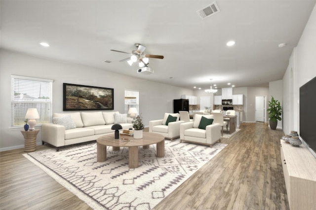 living room with ceiling fan with notable chandelier and light hardwood / wood-style flooring