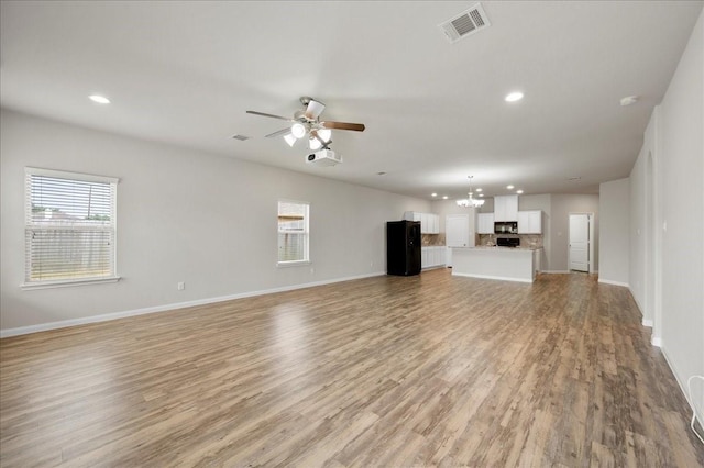 unfurnished living room with plenty of natural light, light hardwood / wood-style floors, and ceiling fan with notable chandelier