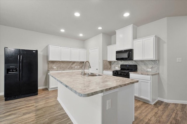 kitchen featuring sink, black appliances, light hardwood / wood-style flooring, white cabinetry, and an island with sink