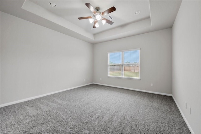 empty room with a raised ceiling, ceiling fan, and carpet flooring