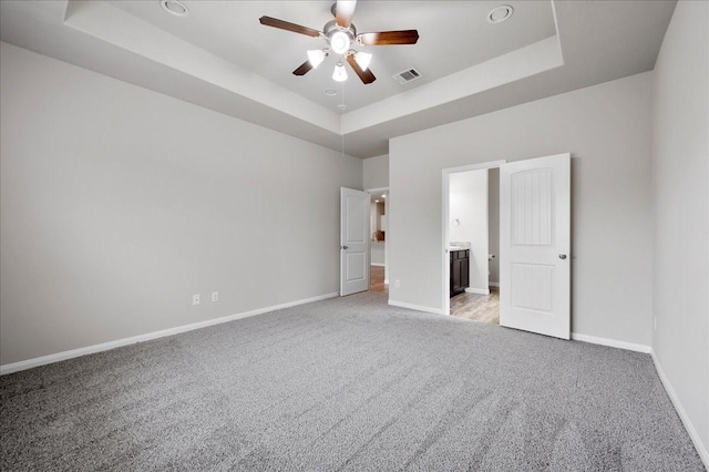 unfurnished bedroom featuring a tray ceiling, connected bathroom, ceiling fan, and light carpet