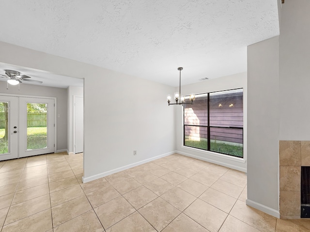 unfurnished dining area with light tile patterned flooring, ceiling fan with notable chandelier, a textured ceiling, and french doors